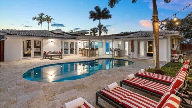 Zona junto a la piscina con sillones de descanso, una piscina y un porche cubierto con bar.