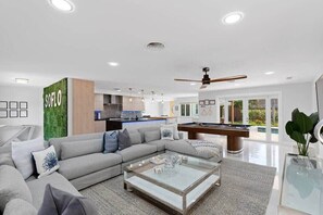A modern living room with a sofa, coffee table, and a pool table.