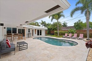 A modern outdoor pool area with a curved pool, a covered patio, and lounge chairs.