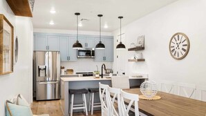 A modern kitchen with light blue cabinets, stainless steel appliances, and pendant lighting. - Anchor Oasis: Desert Color Lagoon + Beaches (St. George)