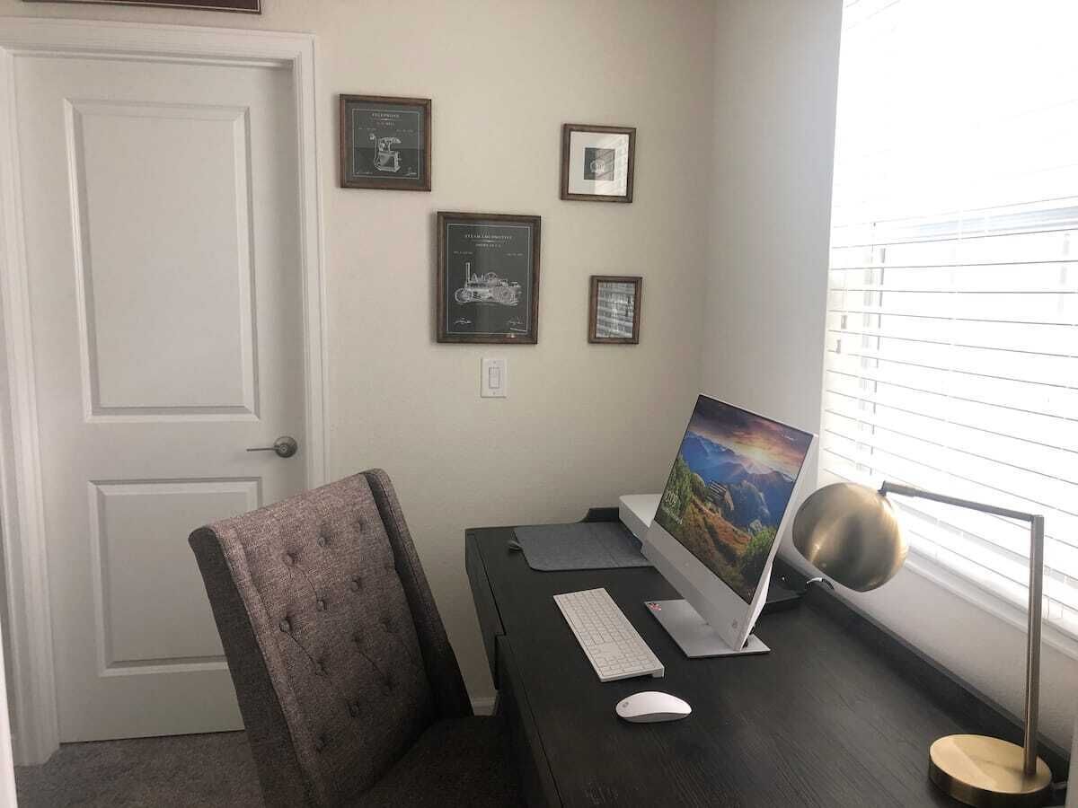 A home office with a desk, computer, chair, and framed pictures on the wall.