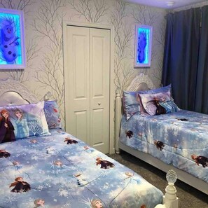 A bedroom with two beds, each with a 'Frozen' themed duvet cover, a white wardrobe, and a door with a frosted glass panel.