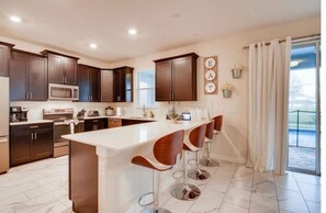 A modern kitchen with dark wooden cabinets, a white island with bar stools, and a view of the outdoors through large windows.