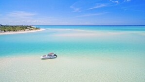 A boat on a clear turquoise sea with a sandy beach and greenery in the background. - LUXURY BEACHFRONT Villa on EXQUISITE BEACH, crystal WATER. IN SANDCASTLE ESTATES (Sandy Point)