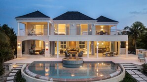 A two-story house with a pool, outdoor seating, and a well-lit interior. - LUXURY BEACHFRONT Villa on EXQUISITE BEACH, crystal WATER. IN SANDCASTLE ESTATES (Sandy Point)