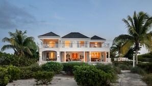 Ein zweistöckiges Strandhaus mit Balkon, umgeben von tropischer Vegetation und Palmen.