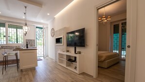 A modern kitchen with a dining area, a living room with a TV, and a bedroom with a view. - Cozy apartment with garden equipped with every comfort 10min from the center (Roma)