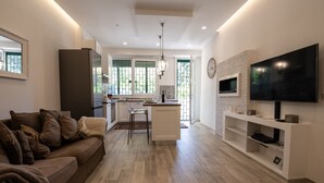A modern kitchen with a central island, a dining area with a brown sofa, and a flat-screen TV mounted on the wall. - Cozy apartment with garden equipped with every comfort 10min from the center (Roma)
