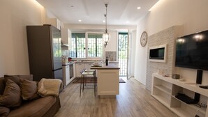 A modern kitchen with a central island, a dining area with a sofa, and a TV mounted on the wall. - Cozy apartment with garden equipped with every comfort 10min from the center (Roma)
