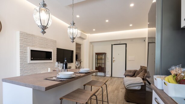 A modern kitchen with a central island, bar stools, and pendant lighting. - Cozy apartment with garden equipped with every comfort 10min from the center (Roma)