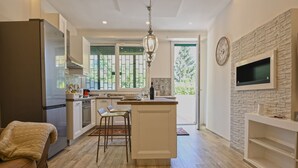 A modern kitchen with a central island, a dining area with chairs, a sofa, and a TV mounted on a stone wall. - Cozy apartment with garden equipped with every comfort 10min from the center (Roma)