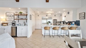 A modern kitchen with white cabinetry, a central island with bar stools, and a decorative sign on the wall. - WATERCOLOR SKY BEACH HOUSE - Well-appointed house with great location!! (Crystal Beach)