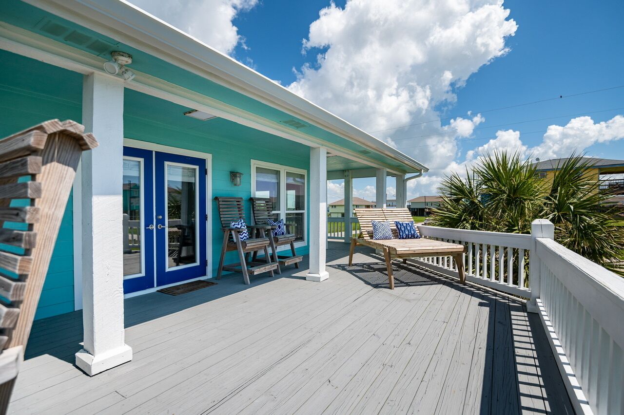 A covered porch with a teal and white color scheme, wooden furniture, and a view of the surrounding area.