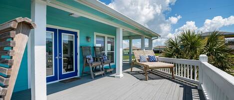 A covered porch with a teal and white color scheme, wooden furniture, and a view of the surrounding area.