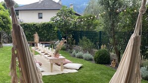 Un jardin verdoyant avec une table de pique-nique installée sur une pelouse, entouré de végétation et avec une maison en arrière-plan.