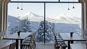 Un espace repas offrant une vue sur les montagnes enneigées grâce à de grandes fenêtres.