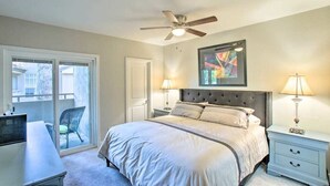 A bedroom with a bed, two bedside tables with lamps, a ceiling fan, a window, and a door.