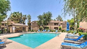 A swimming pool with lounge chairs and umbrellas, surrounded by buildings with a Mediterranean architectural style.
