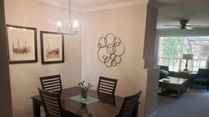 A dining area with a dark wooden table and chairs, framed pictures on the wall, and a decorative metal piece.