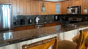 A modern kitchen with wooden cabinets, stainless steel appliances, granite countertops, and pendant lighting. - Entire condominium with a pool view, steps from the beach (Sunny Isles Beach)
