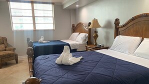 A hotel room with two beds, a wooden headboard, a nightstand with a lamp, and a chair. - Entire condominium with a pool view, steps from the beach (Sunny Isles Beach)