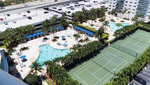 An aerial view of a hotel with a swimming pool, tennis court, and parking area. - Entire condominium with a pool view, steps from the beach (Sunny Isles Beach)
