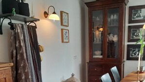 Zona pranzo con tavolo in legno, sedie, un pensile con ante in vetro e un attaccapanni.