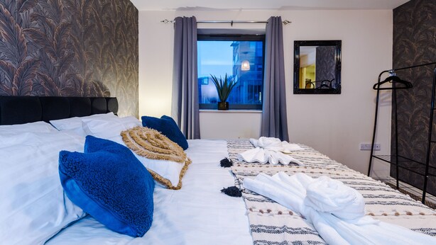 Une chambre d’hôtel avec un grand lit, une fenêtre avec des rideaux, un miroir et un porte-vêtements.