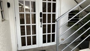 Une porte blanche avec le chiffre « 3 » au-dessus, une main courante en métal et un paillasson noir sur un sol carrelé.