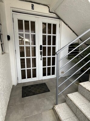 Une porte blanche avec le chiffre « 3 » au-dessus, une main courante en métal et un paillasson noir sur un sol carrelé.