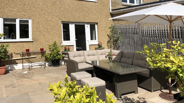 A patio area with a glass-top table, cushioned seating, potted plants, and a wooden fence.
