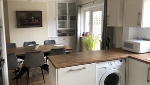 A compact kitchen with a washing machine, a microwave, and a dining area with a table and chairs.