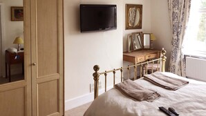 A bedroom with a bed, a TV mounted on the wall, a dresser, a mirror, and a window with curtains.