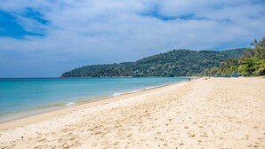 Uma praia com areal dourado, águas azul-claras e uma colina com árvores ao fundo.