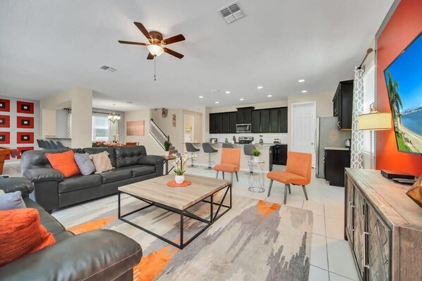 A modern living room with a sofa, coffee table, and chairs. There is a kitchen area with cabinets and appliances in the background.