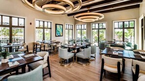 Un comedor amplio con varias mesas y sillas, ventanas grandes y un diseño moderno en el techo.