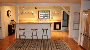 Uma cozinha moderna com uma ilha central, banquetas, piso de madeira e vista para a sala de jantar.