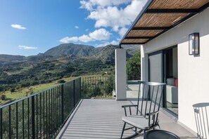 A balcony with a view of a mountainous landscape, a chair, and a table.