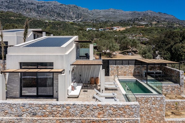 Una villa moderna con piscina, pareti in pietra e vista sulle montagne.