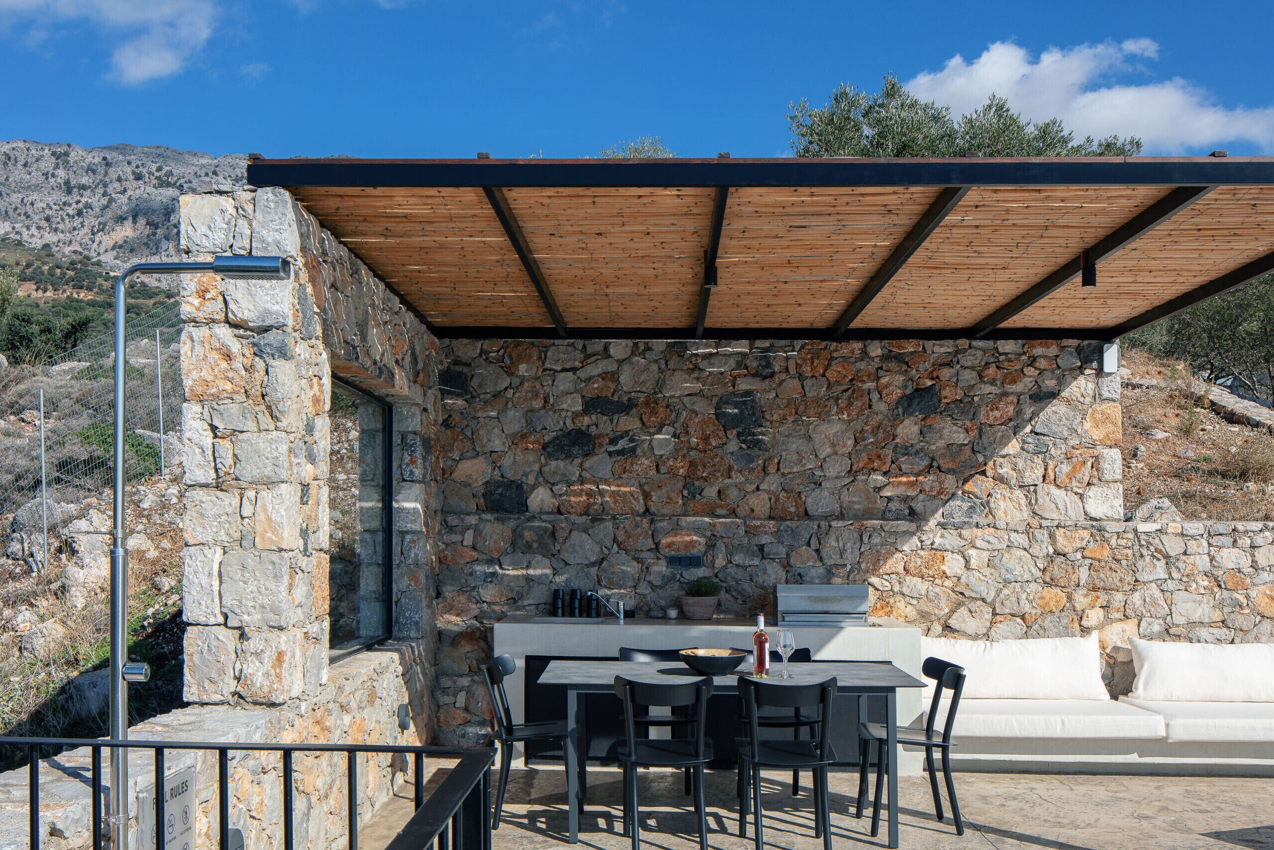 Eine Steinmauer mit Holzdach, Außenbereich mit Sitzgelegenheiten und einem weißen Sofa.