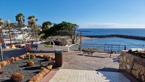 Un chemin pavé mène à une plage où se trouvent une poubelle, des bancs et un panneau indiquant « Le Château ».