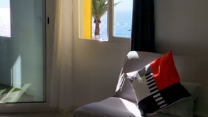 Une chambre avec un lit, une fenêtre donnant sur la mer et une porte qui mène à un espace extérieur.