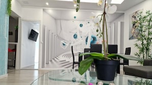 Un salon moderne avec une table basse en verre, une plante en pot et un escalier doté de rampes blanches.