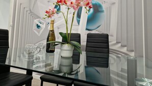 Un espace repas moderne avec une table en verre, des chaises noires, un vase rempli de fleurs roses et une bouteille de champagne.