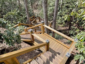 A wooden deck with metal railings and benches, surrounded by trees and foliage. - Cozy Mountain Cabin Nestled on 3.5 Acres - Multi-Tier Deck, Creek Access! (Clyde)