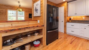 A kitchen with wooden walls, a stainless steel refrigerator, and wooden shelves with cookware. - Cozy Mountain Cabin Nestled on 3.5 Acres - Multi-Tier Deck, Creek Access! (Clyde)