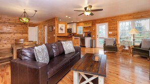 A spacious living room with a brown leather sofa, a wooden coffee table, and a ceiling fan. - Cozy Mountain Cabin Nestled on 3.5 Acres - Multi-Tier Deck, Creek Access! (Clyde)
