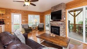 A cozy cabin interior with a leather sofa, a stone fireplace, a television, and a wooden ceiling fan. - Cozy Mountain Cabin Nestled on 3.5 Acres - Multi-Tier Deck, Creek Access! (Clyde)