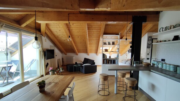 A spacious living area with a wooden ceiling, a dining table with chairs, and a kitchen area with stools. - Cozy stay in the heart of Mondovi (Mondovi')