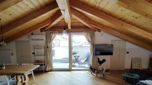 An attic room with wooden beams, a dining table, chairs, a TV, and a rooster decoration. - Cozy stay in the heart of Mondovi (Mondovi')